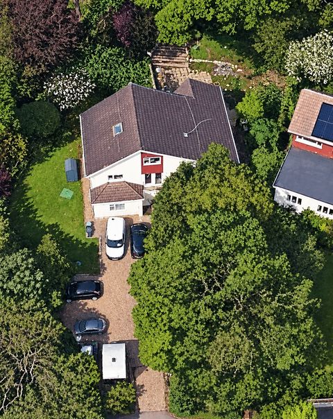 Aerial photograph of 1 Ferndale: a large white-rendered house with a dark tiled roof, surrounded by mature trees and gardens, with cars and a caravan parked along a gravel drive that runs down to the road.